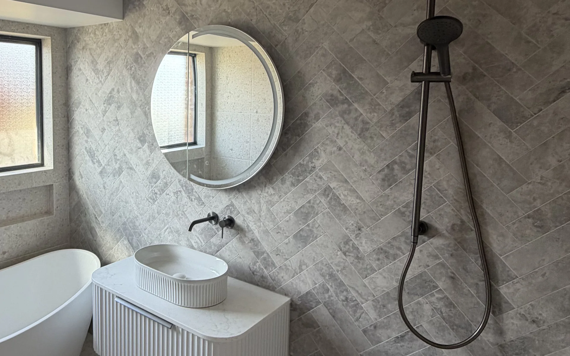 Renovated bathroom with a wall hung vanity, round mirror and tiled shower