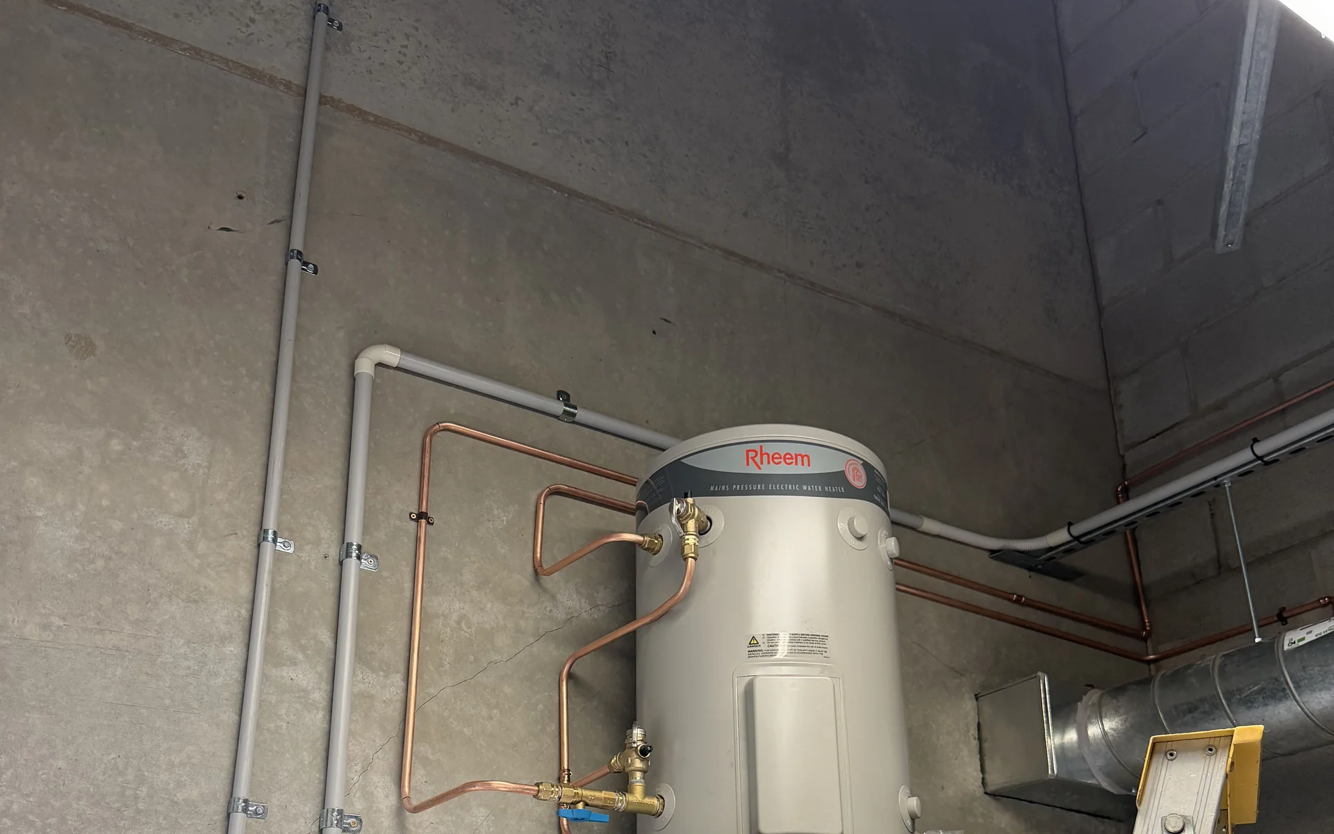 Hot water unit installed on a bracket with copper pipework