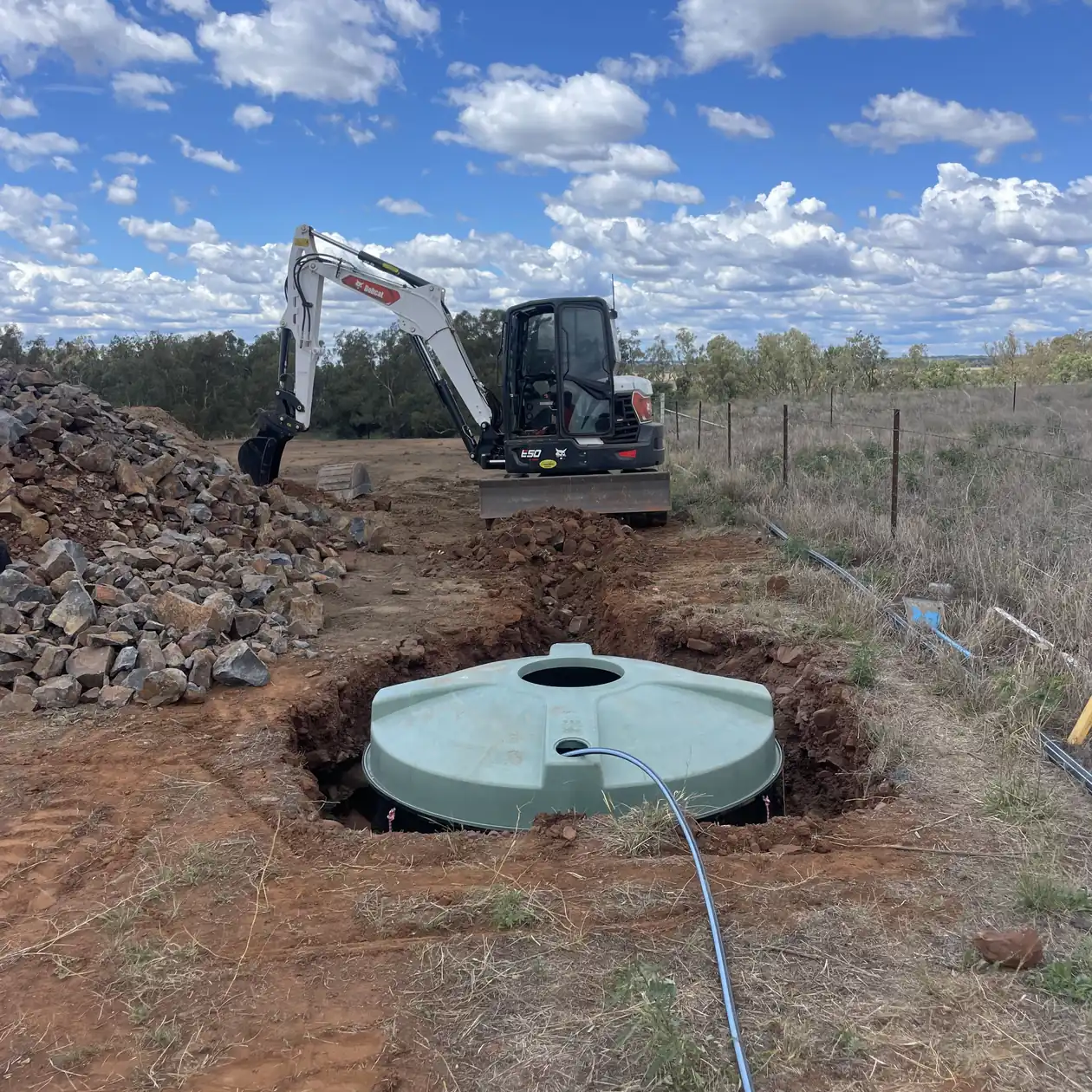 Excavator lowering a tank into a prepared excavation