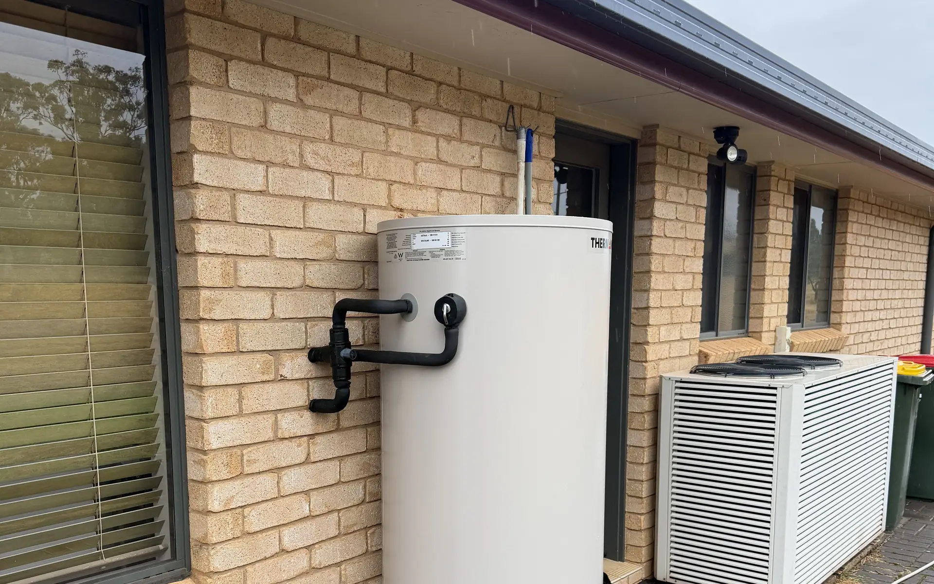 Storage hot water unit installed against the brick wall of a house