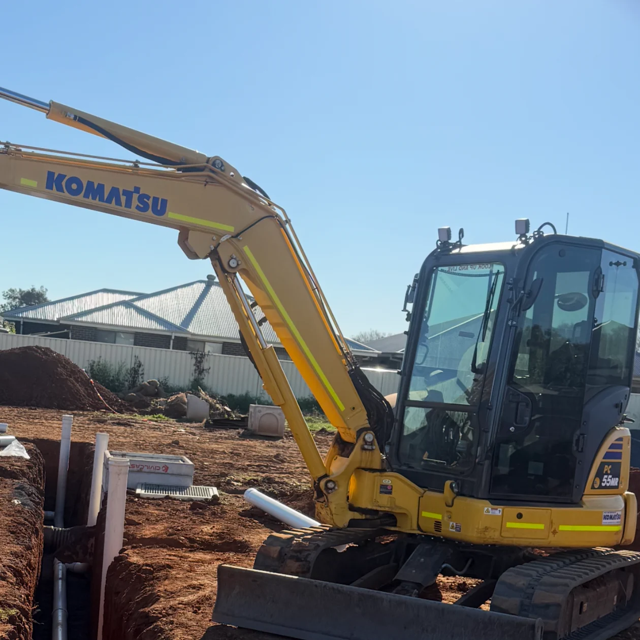 Excavator on a residential site beside an open trench with drainage pipework laid in it