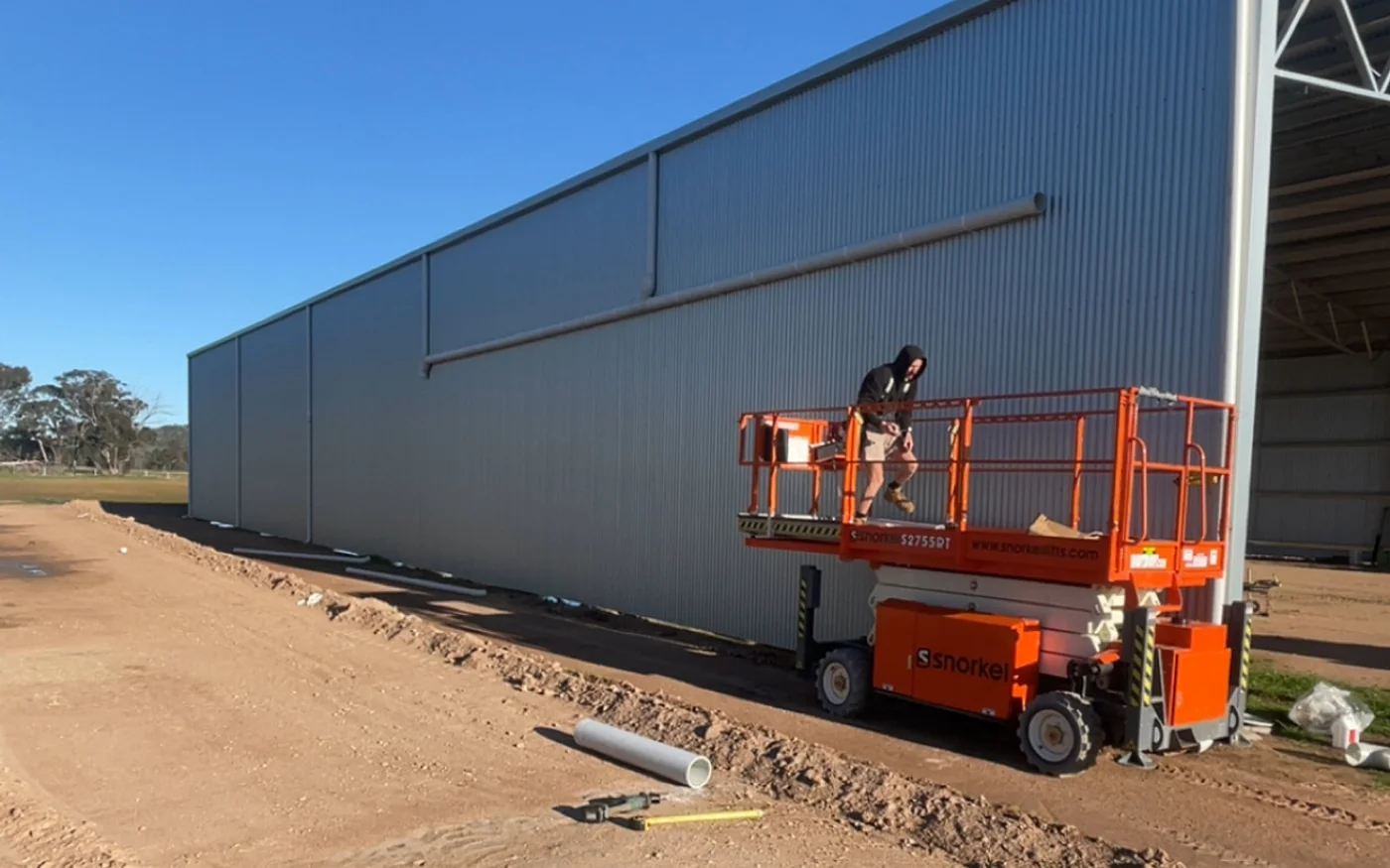 Tradesman installing metal wall cladding on a large shed from a scissor lift