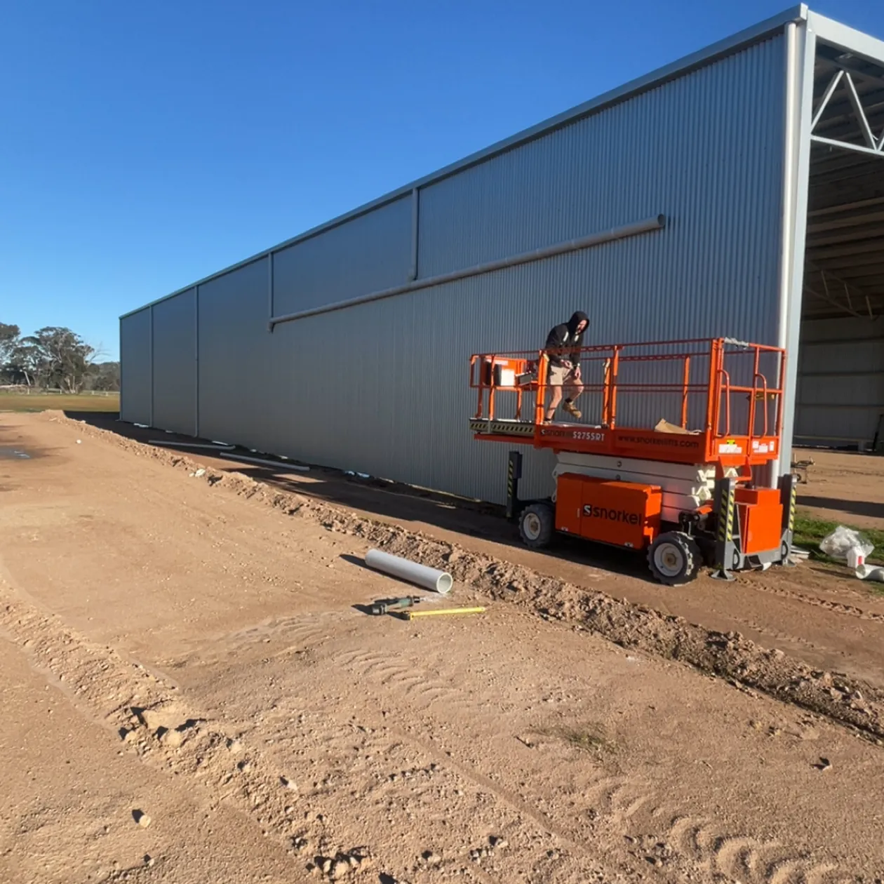 Metal wall cladding being installed on a large shed from a scissor lift