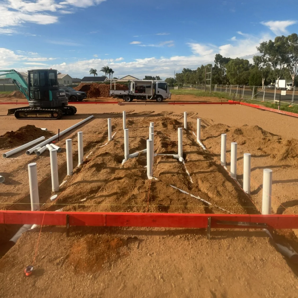 Sanitary drainage rough-in laid out on a new home site with an excavator and work truck