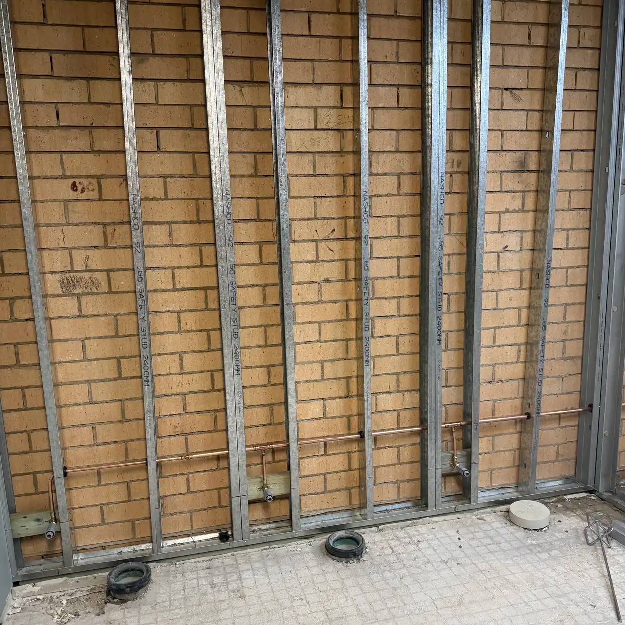 Copper water pipework and floor wastes roughed in behind a steel stud wall