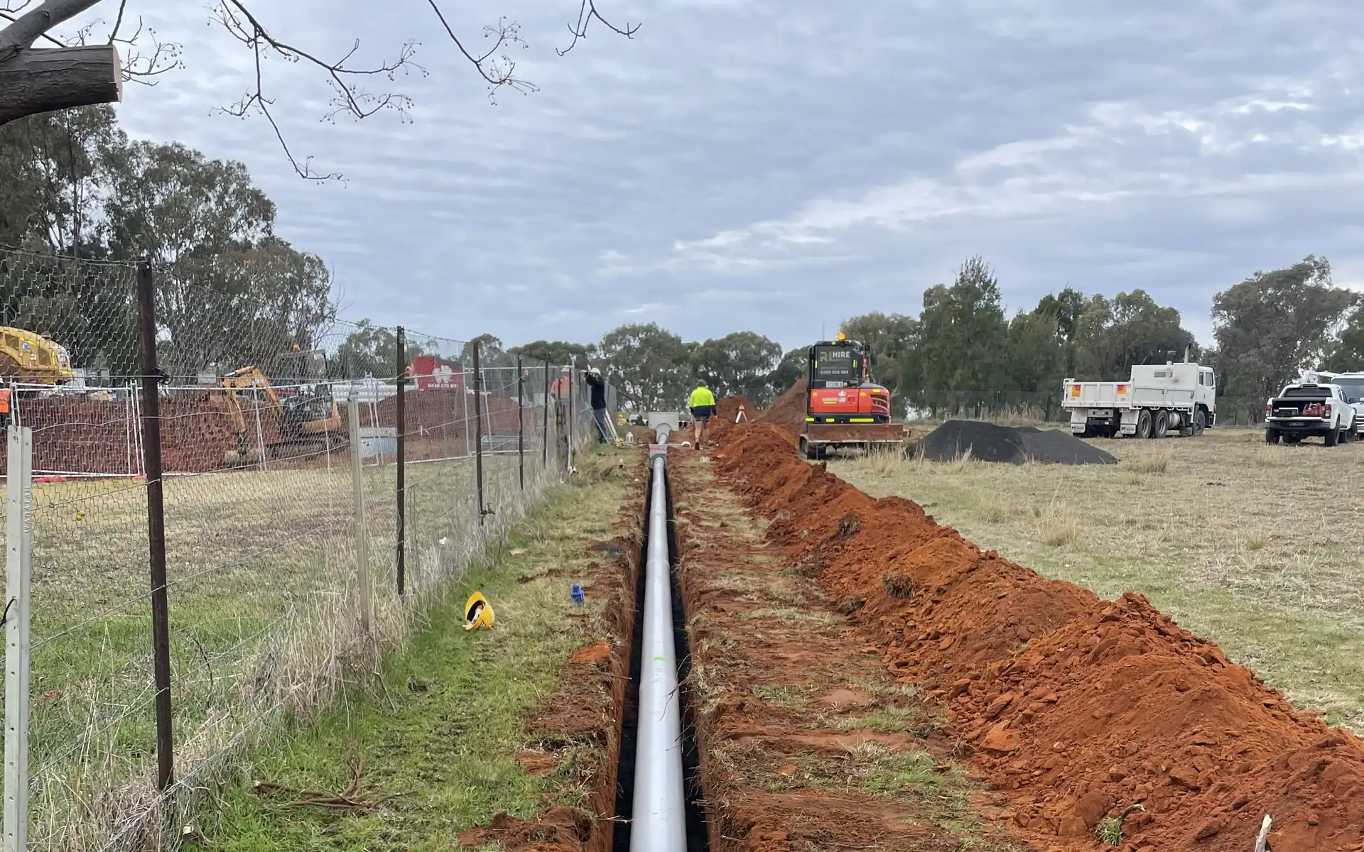 Large sewer main being laid in an open trench with an excavator on site