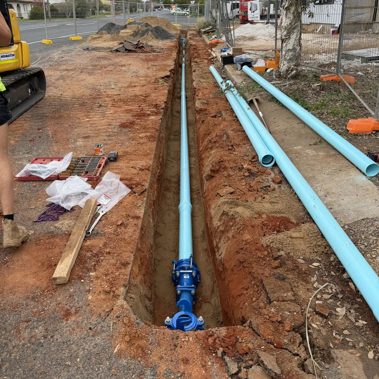 New water main and valve installed in a street trench with pipe stacked ready to lay